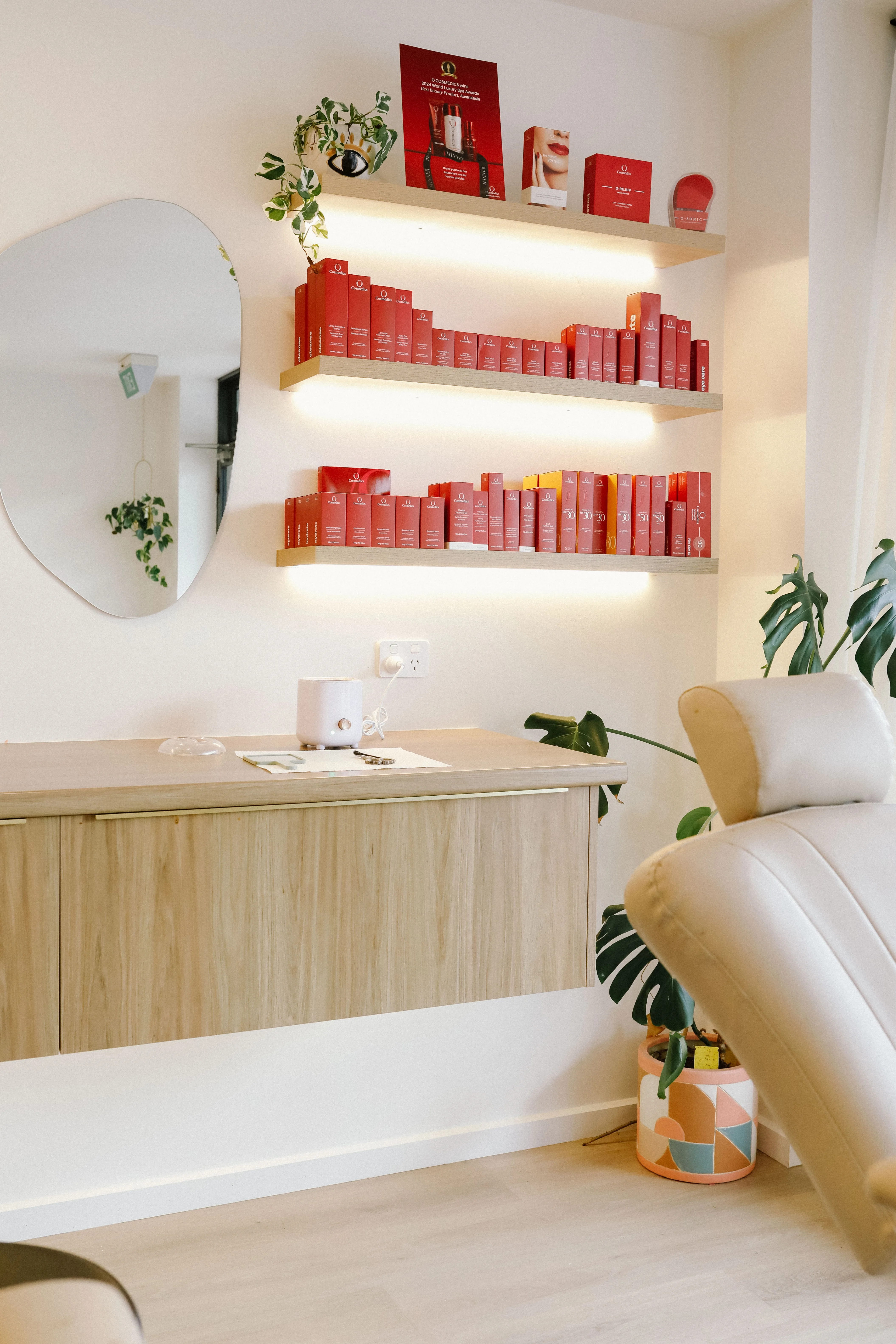 Treatment room at LUNA showing lit oak shelves of O Cosmedics products alongside a cream treatment bed and monstera plant