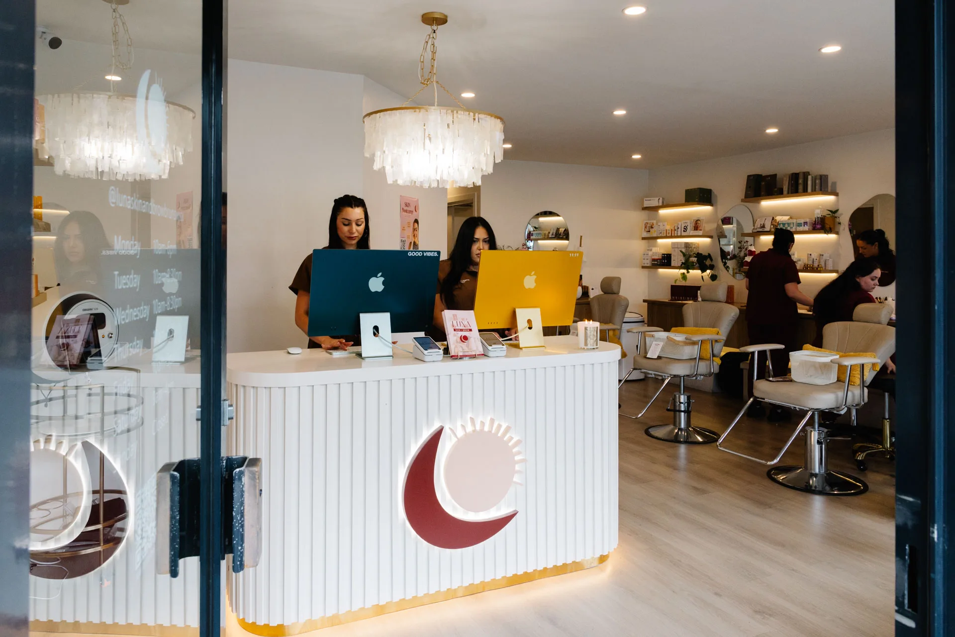 LUNA Skin + Brow reception area seen through the front doorway, showing the backlit crescent and sun mark above the fluted white desk