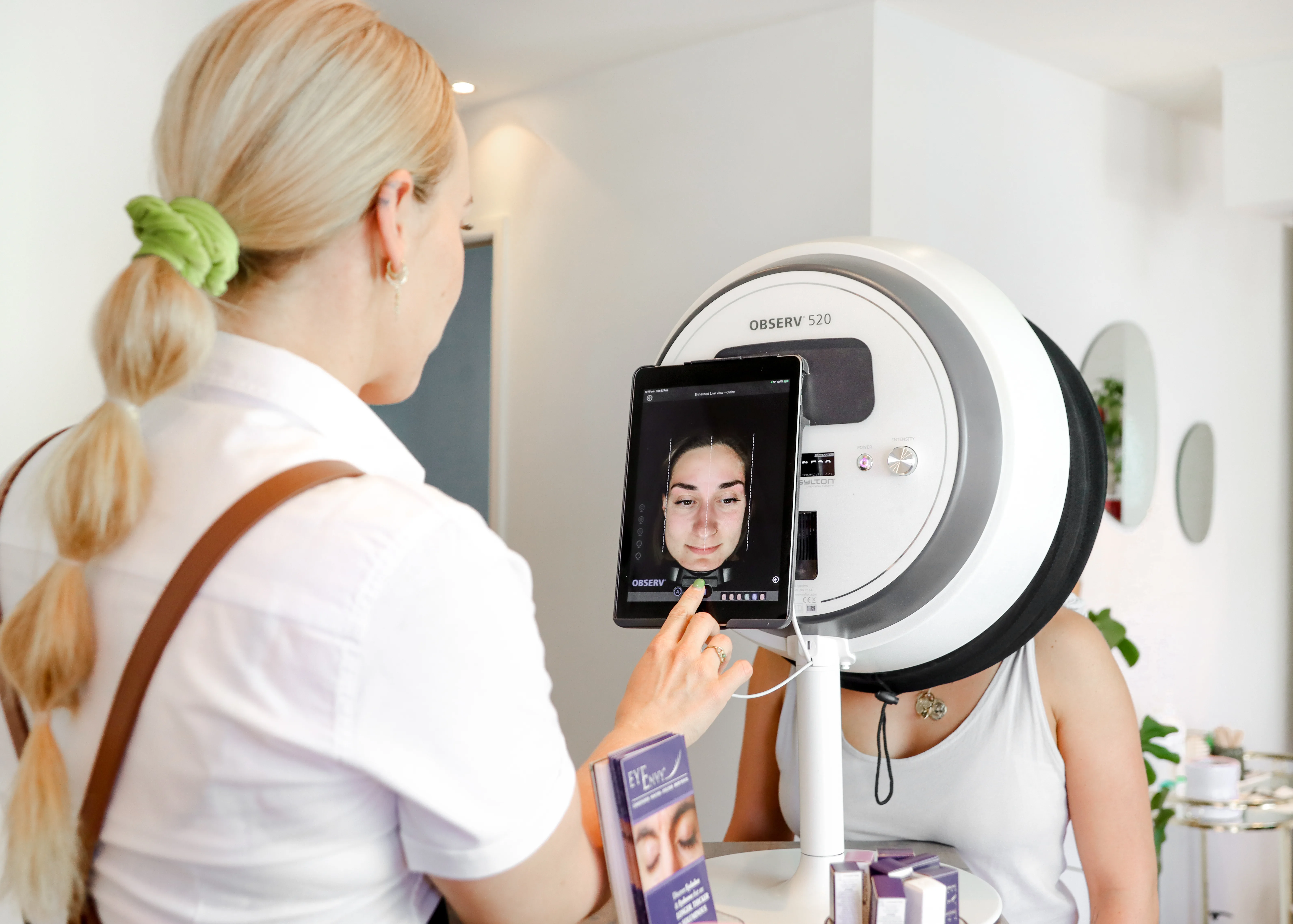 LUNA therapist operating an OBSERV 520 skin-analysis unit, client's live face scan visible on the mounted iPad